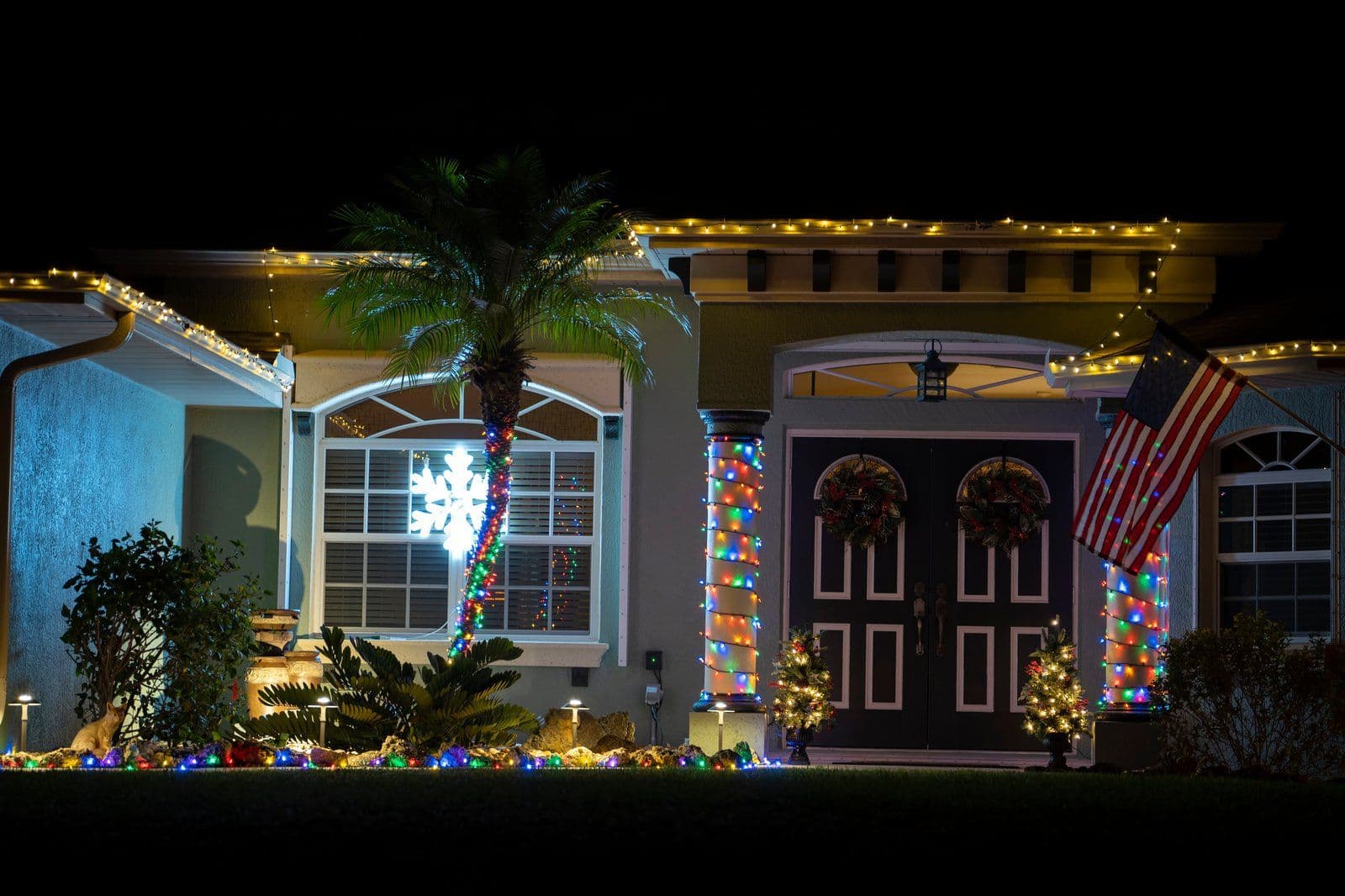 Front entry at night with lit wreaths on double doors and wrapped columns